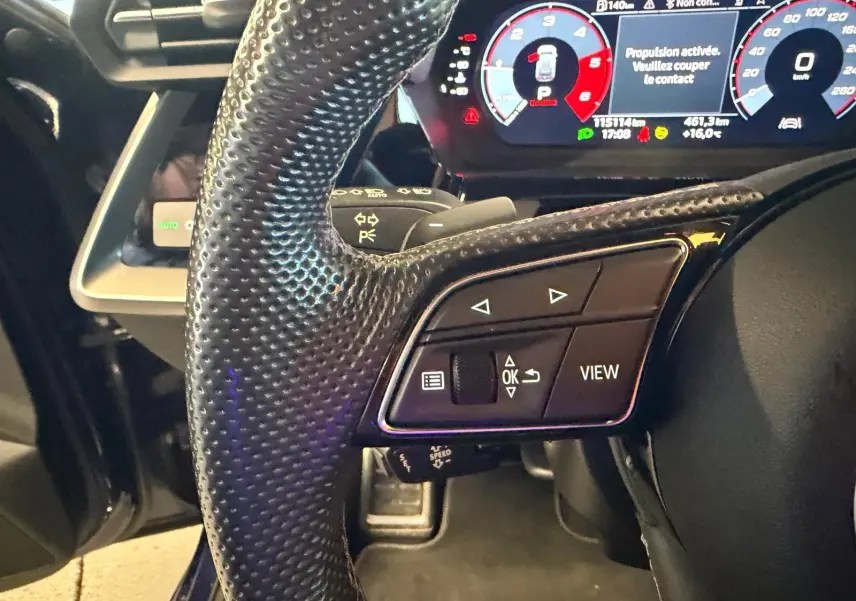 Gros plan sur le volant noir perforé et le tableau de bord numérique d’une Audi A3 bleu, version 2.0 TDI 150 S-TRONIC S-LINE.