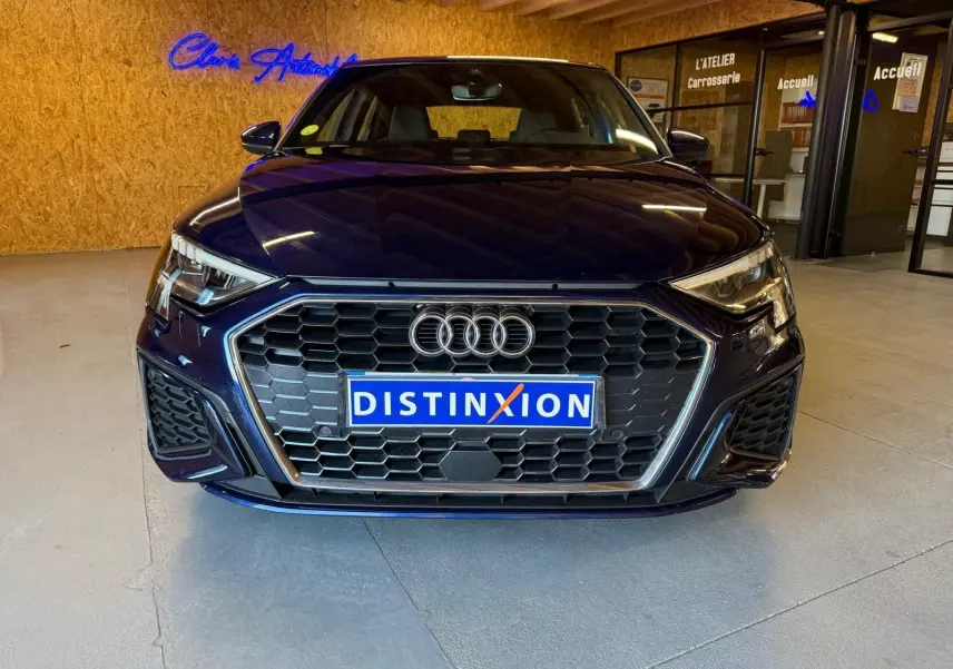 Vue frontale d'une Audi A3 2.0 TDI S-Line bleu foncé avec calandre hexagonale et logo Audi visible en intérieur.