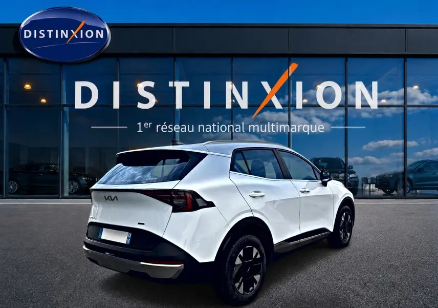 Vue 3/4 arrière droite d'un KIA Sportage blanc 2026 devant une vitrine avec logo Distinxion.