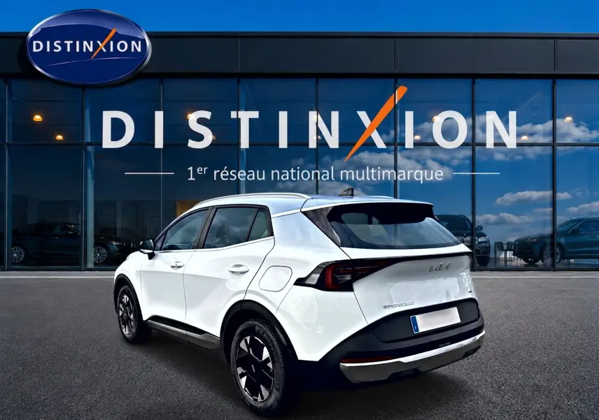 Vue 3/4 arrière droite d'un KIA SPORTAGE blanc 2026 avec jantes alu noires devant un showroom Distinxion.
