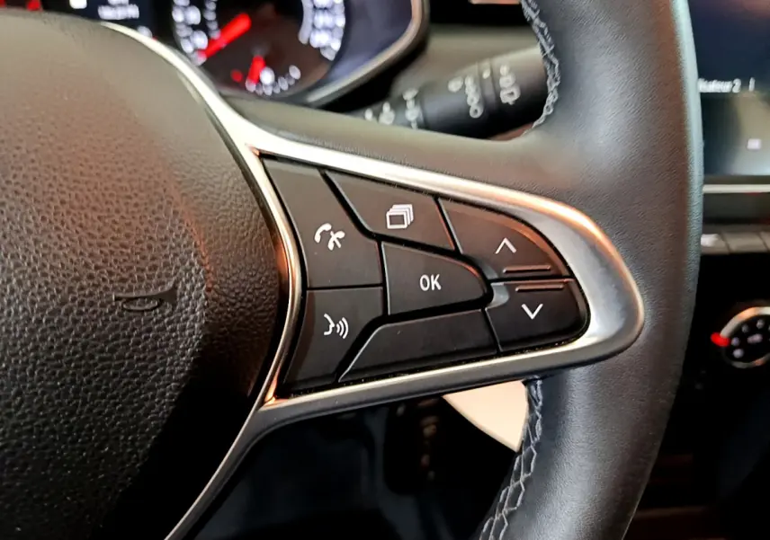 Gros plan sur les commandes multifonctions du volant cuir noir de la Renault Clio Business blanche de 2021.