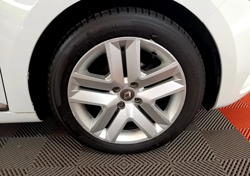 Gros plan sur la roue avant gauche d'une Renault Clio Business blanche, jante alliage à cinq branches doubles.