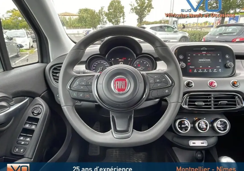 Vue intérieure centrée sur le volant sport noir de la Fiat 500X gris, avec tableau de bord et écran tactile visible.