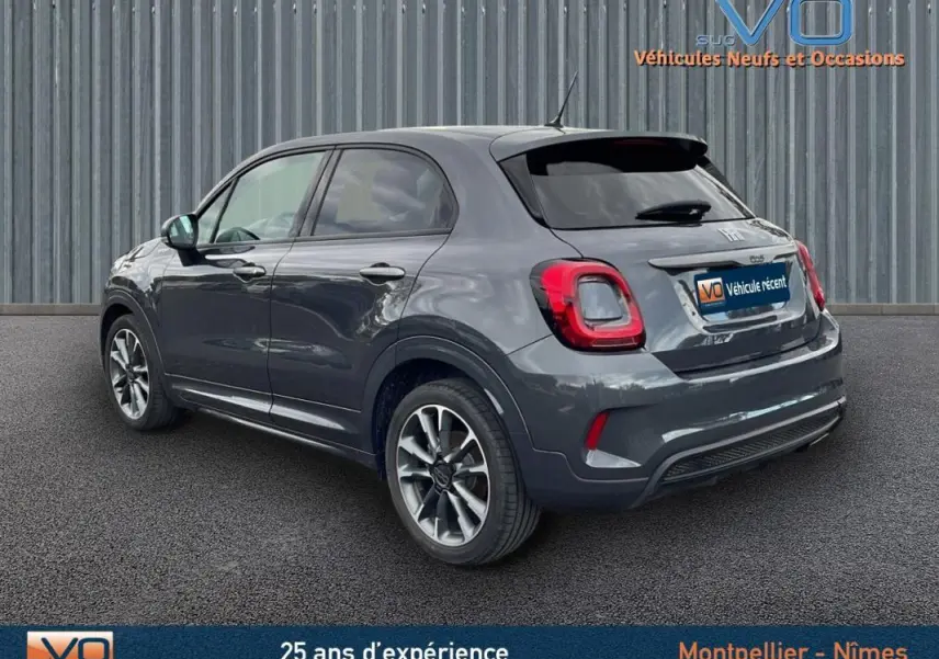 Vue 3/4 arrière droite d'une FIAT 500X gris métallisé avec jantes alliage 18 pouces sur fond urbain.
