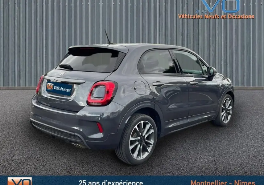 Vue 3/4 arrière droite d'une FIAT 500X gris métallisé avec jantes alliage 18 pouces sur parking extérieur.
