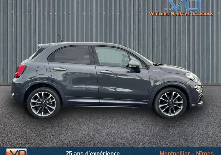Profil côté gauche d'une FIAT 500X gris métallisé version Sport avec jantes alliage 18 pouces sur fond urbain.