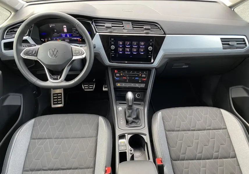 Vue intérieure frontale du tableau de bord et volant Volkswagen Touran 2025 avec sellerie grise et écran tactile central.