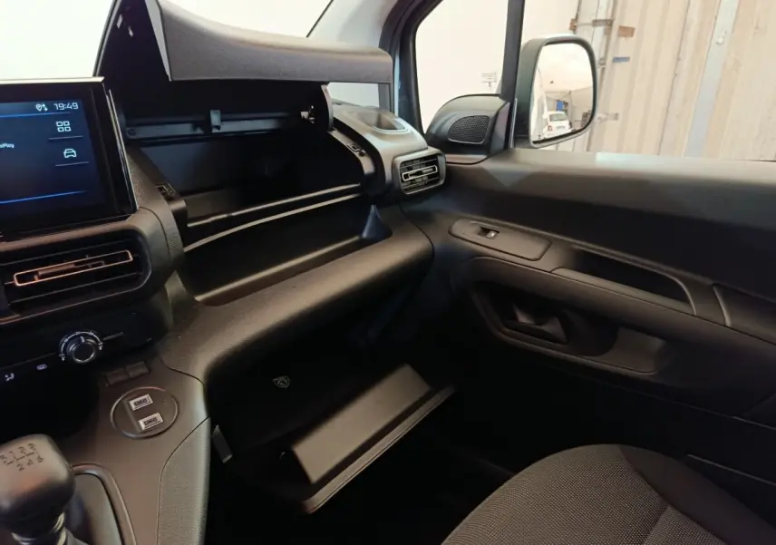 Vue intérieure côté passager du Peugeot Partner blanc 2026, montrant tableau de bord et boîte à gants ouverte.