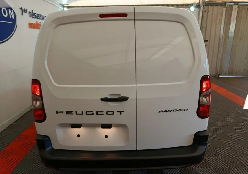 Vue arrière d’un utilitaire Peugeot Partner blanc avec portes battantes et feux arrière allumés en intérieur.