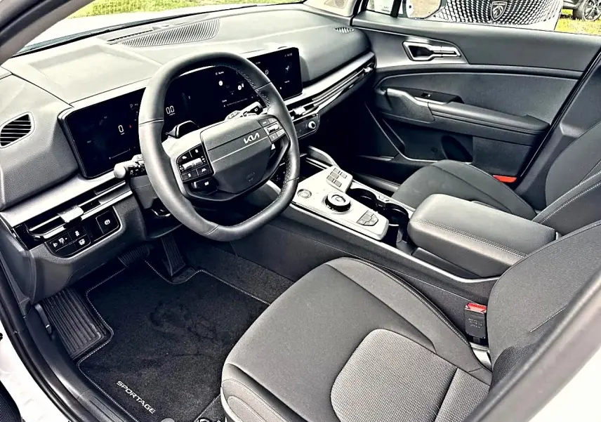Vue intérieure côté conducteur du Kia Sportage 2026 hybride, montrant le volant cuir multifonction et la console centrale moderne.
