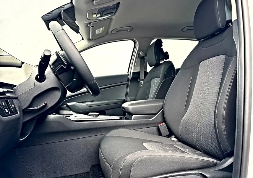 Intérieur côté conducteur du Kia Sportage 1.6 hybride 2026, sièges noirs avec accoudoir central et volant multifonction.