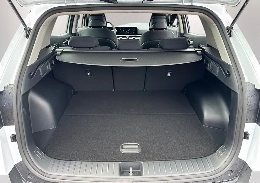 Coffre ouvert vu de l'arrière d'un KIA Sportage blanc 2026, avec cache-bagages et banquette arrière noire.