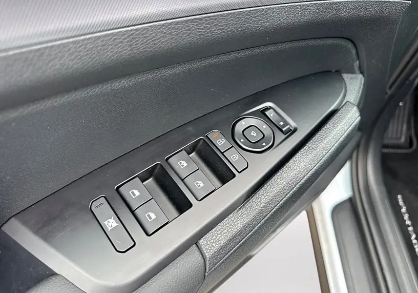 Gros plan sur la commande des vitres et rétroviseurs côté conducteur du Kia Sportage blanc, avec texture cuir noire.