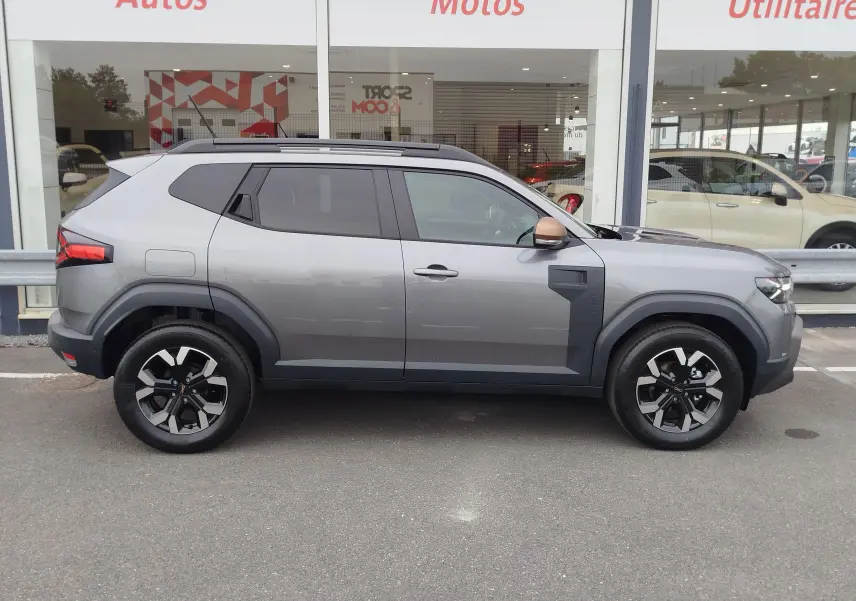 Profil côté droit du Dacia Duster 2025 gris schiste avec jantes noires et coques de rétroviseurs couleur cuivre.