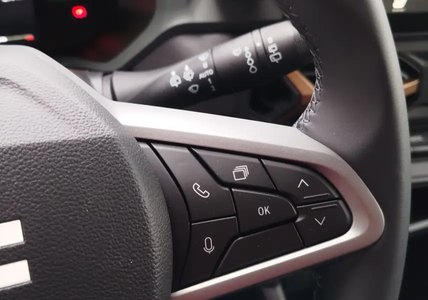 Gros plan sur les commandes multifonctions noires et argentées du volant du Dacia Duster 2025, intérieur gris.