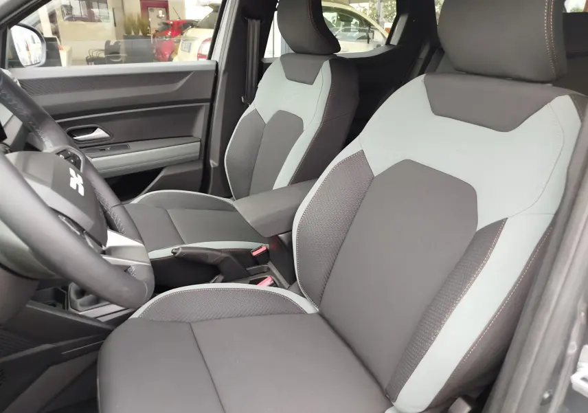 Vue intérieure du Dacia Duster 2025 montrant les sièges avant bicolores gris clair et foncé avec surpiqûres contrastées.