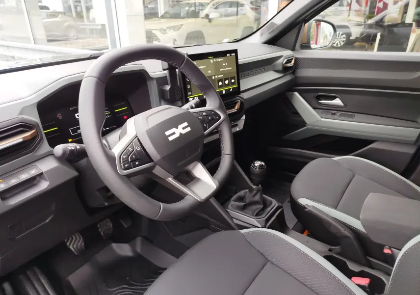 Vue intérieure côté conducteur du Dacia Duster 2025, tableau de bord moderne avec écran tactile et volant multifonction noir.