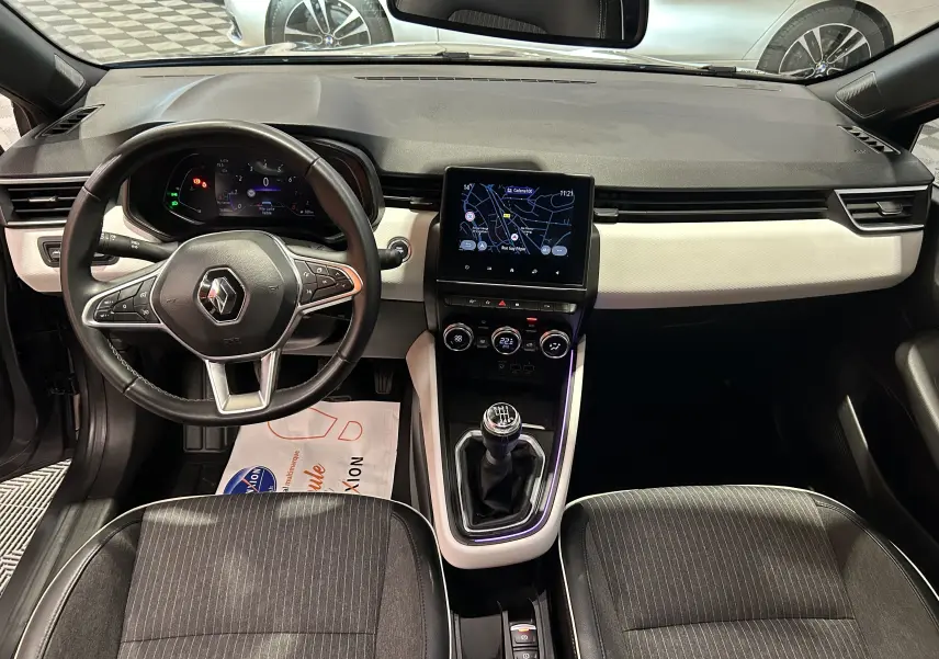 Vue intérieure avant de la Renault Clio V TCe 90 TECHNO 2023, tableau de bord noir et beige avec écran tactile et boîte manuelle.