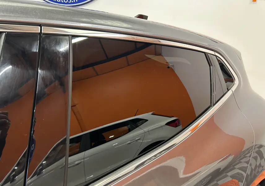 Reflet d'une Renault Clio V gris 3/4 arrière droit, mettant en valeur la ligne fluide et la vitre latérale teintée.