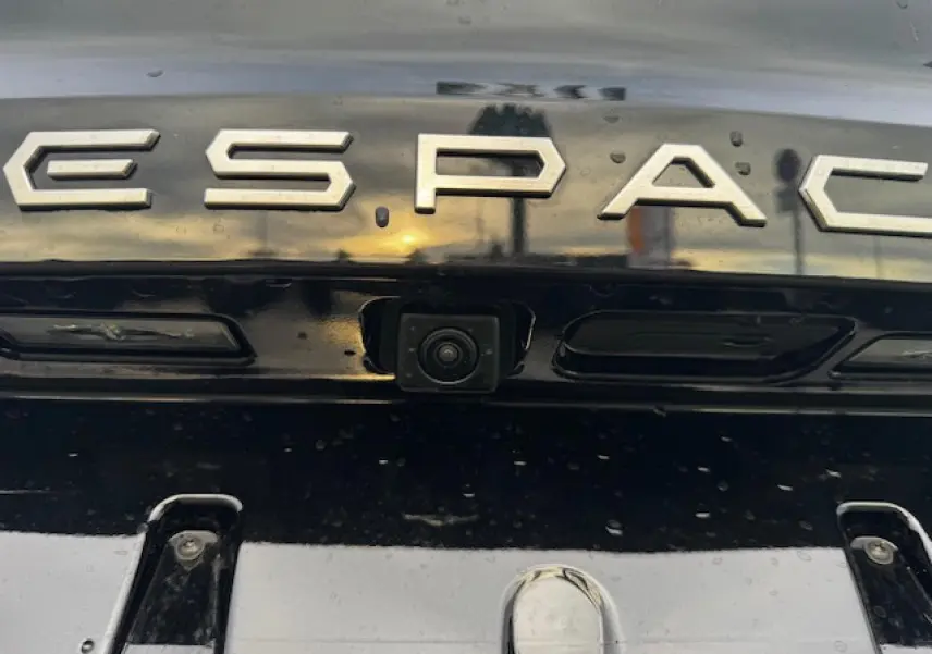 Gros plan sur la caméra de recul intégrée sous le logo ESPACE sur la malle arrière noire étoilée du Renault Espace VI.