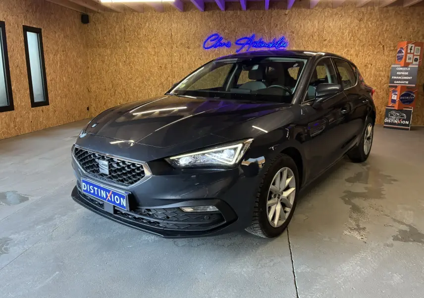 SEAT Leon gris 2021 en 3/4 avant droit dans un showroom avec éclairage intérieur et mur en bois.