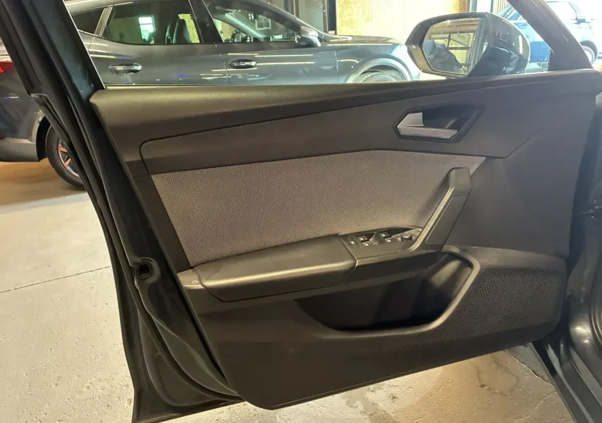 Vue intérieure côté gauche de la porte avant d’une SEAT LEON gris 2021 avec commandes de vitres et poignée noire.