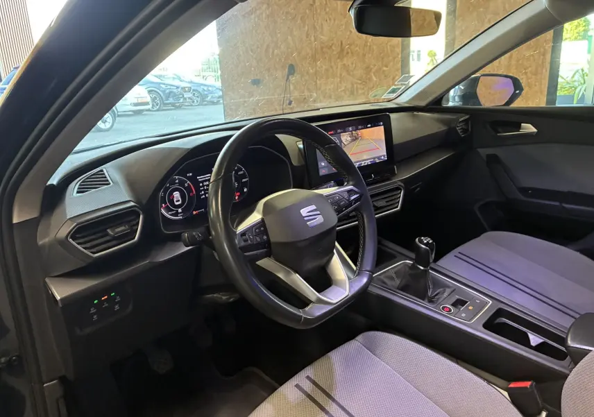 Vue intérieure côté conducteur du SEAT Leon gris 2021, volant multifonction, écran tactile et levier de vitesses manuel visibles.