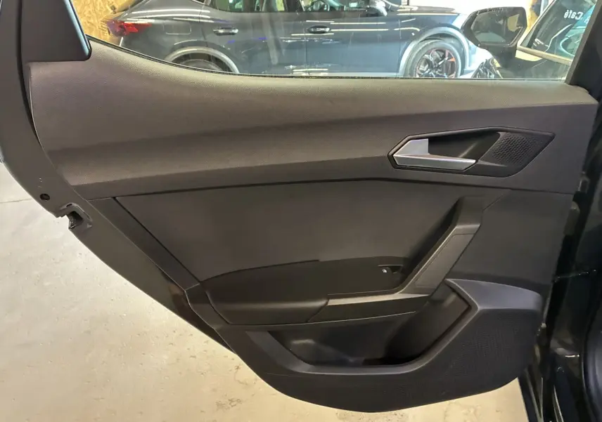 Gros plan sur la porte arrière gauche intérieure noire d'une SEAT Leon gris 2021, avec poignée argentée et haut-parleur intégré.