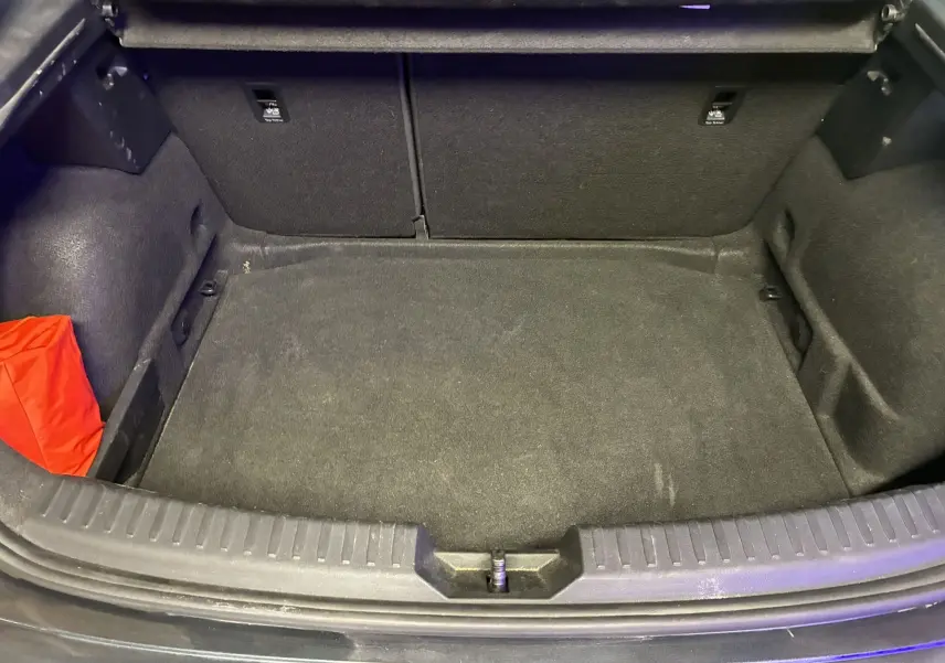 Coffre ouvert vu de dessus d’une SEAT Leon gris 2021, avec tapis noir et un sac rouge dans un coin.