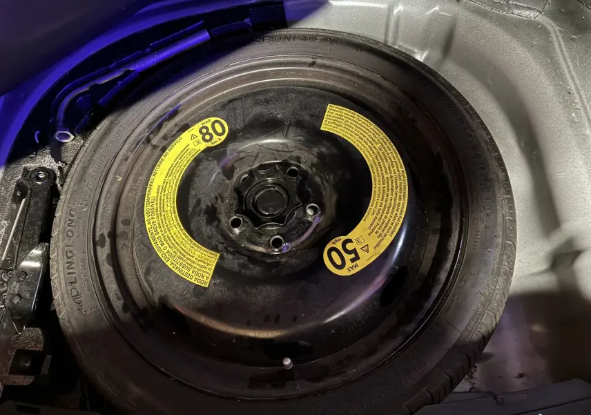 Gros plan sur la roue de secours noire avec étiquettes jaunes dans le coffre d'une SEAT LEON gris 2021.