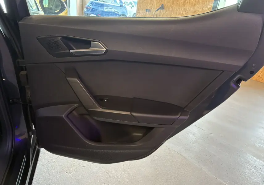 Vue intérieure côté gauche de la porte arrière d’une SEAT LEON gris 2021 avec garniture noire et poignée argentée.