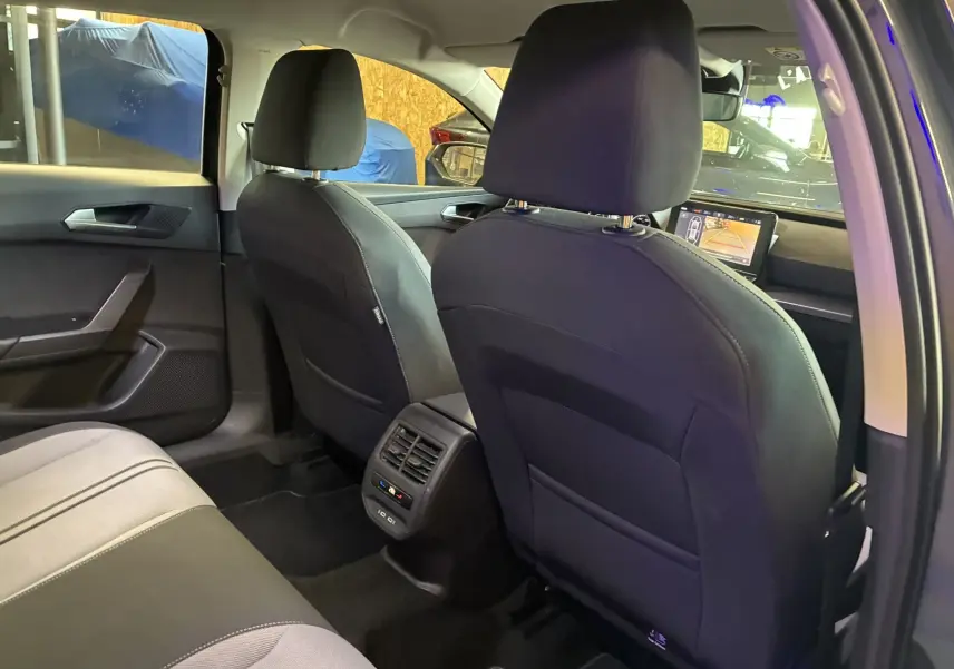 Vue intérieure arrière de la SEAT Leon 2021 gris, montrant les sièges avant en tissu noir et la console centrale avec aérateurs.