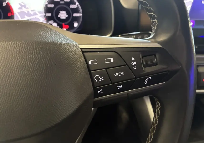 Gros plan sur les commandes au volant côté gauche du SEAT Leon gris 2021, avec boutons multifonctions et volant en cuir noir.