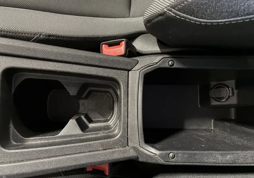 Gros plan intérieur sur la console centrale noire du SEAT LEON 2.0 TDI 115 STYLE avec porte-gobelets et prise 12V.