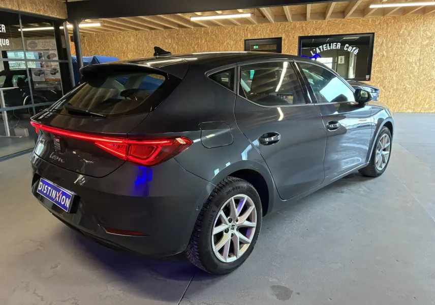 SEAT Leon 2.0 TDI gris vue 3/4 arrière droit, feux arrière allumés et jantes alliage en intérieur showroom.