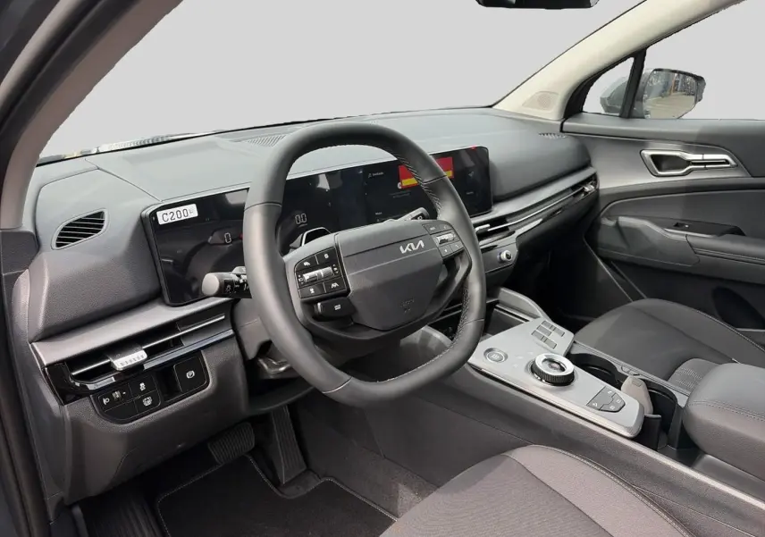 Intérieur avant du Kia Sportage 1.6 hybride 2026, vue côté conducteur, tableau de bord et volant cuir multifonction.