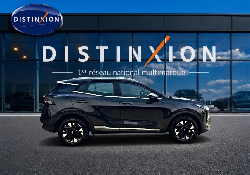 Profil côté gauche du KIA SPORTAGE 1.6 hybride 239 active gris eclipse avec jantes alu noires devant une vitrine Distinxion.