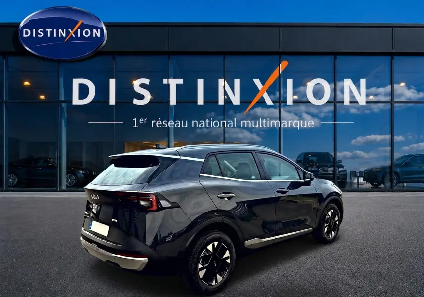 Vue 3/4 arrière droite d'un KIA Sportage gris eclipse 2026 avec jantes alu et feux arrière LED, devant un showroom Distinxion.
