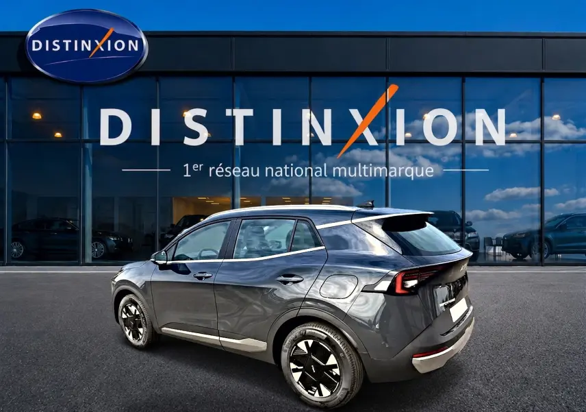 Vue 3/4 arrière droite du KIA SPORTAGE 1.6 hybride gris eclipse avec jantes alu et feux arrière LED, devant un showroom Distinxion.