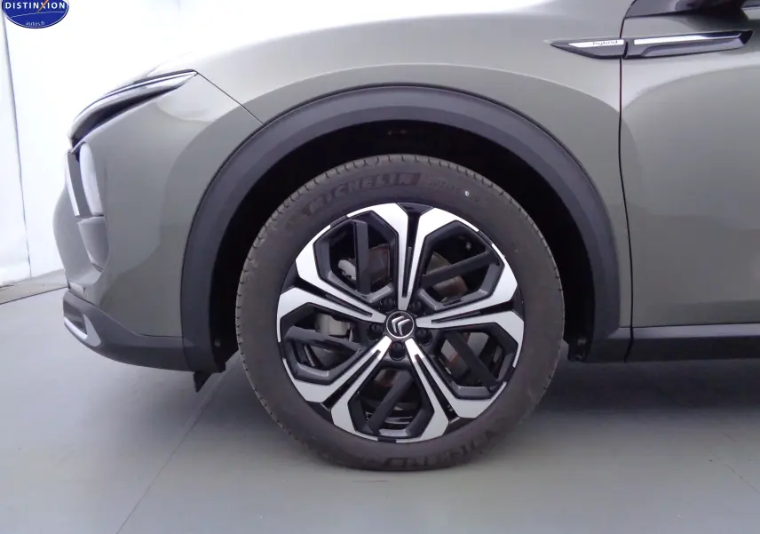 Gros plan sur la roue avant gauche d'une Citroën C5 X gris smart avec jante alliage bicolore et badge Hybrid.