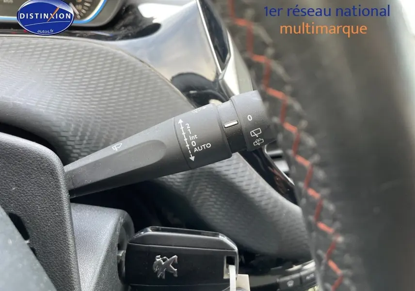 Gros plan sur la commande d’essuie-glace à gauche du volant d’un Peugeot 2008 blanc, intérieur noir avec surpiqûres rouges.