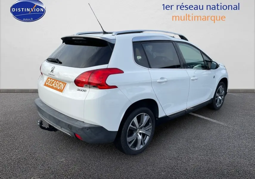 Peugeot 2008 blanc en 3/4 arrière droit, avec barres de toit et attelage visible sur parking.