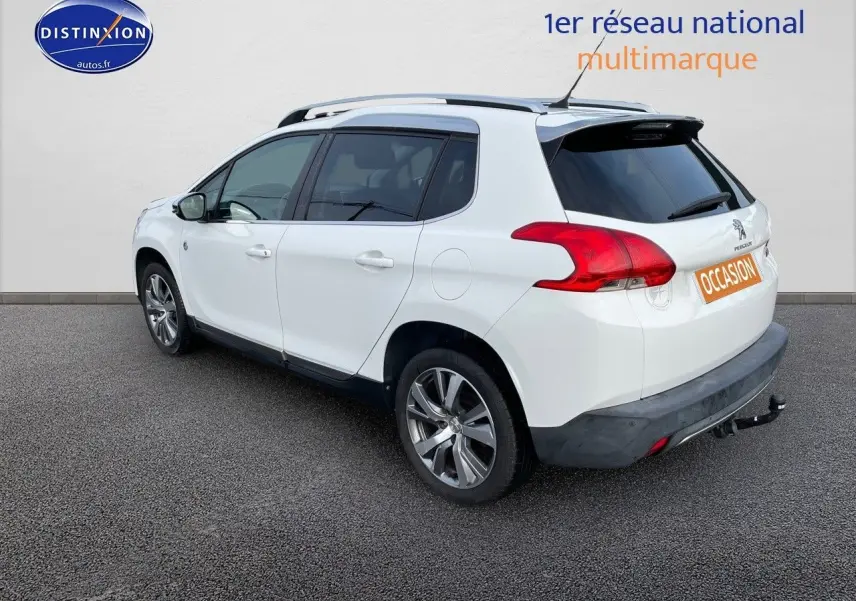 Peugeot 2008 blanc vue 3/4 arrière droit, avec barres de toit et attelage visible sur fond neutre.