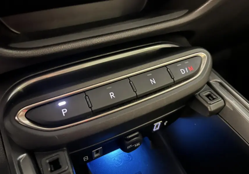 Gros plan sur la console centrale noire de la Fiat 600 Hybrid 2024 avec boutons de boîte auto éclairés et éclairage bleu dessous.