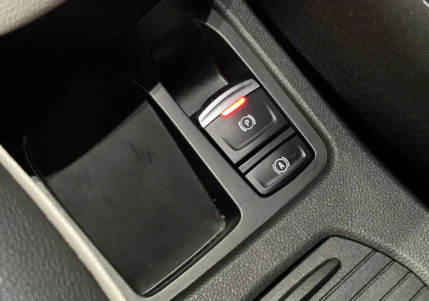 Gros plan sur les commandes de frein à main électronique et d'assistance au démarrage en côte dans l'habitacle noir d'une Renault Clio V rouge.