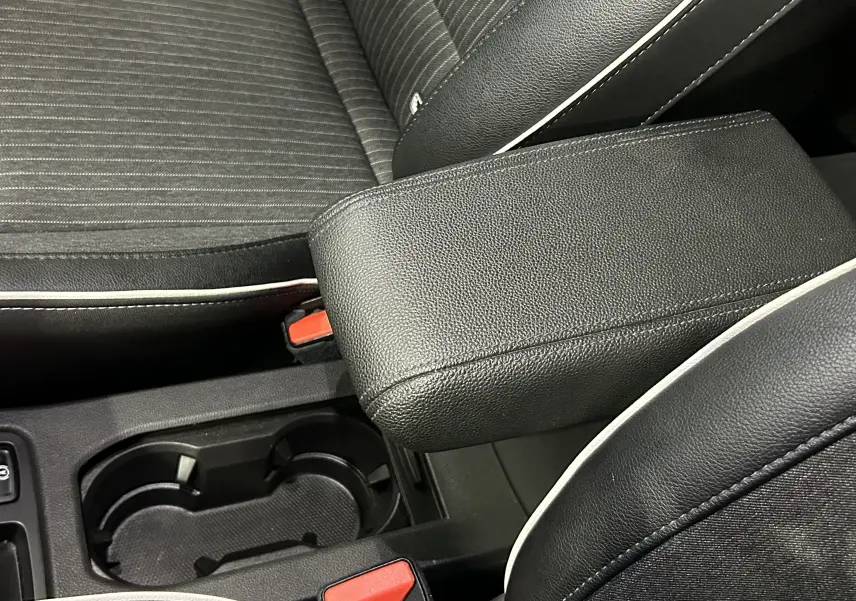 Accoudoir central en cuir noir avec surpiqûres blanches et sièges tissu noir à rayures dans Renault Clio V rouge 2023.