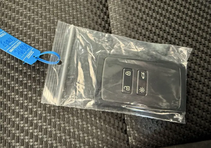 Télécommande noire Renault Espace esprit Alpine 7 places dans pochette plastique sur tissu gris foncé.