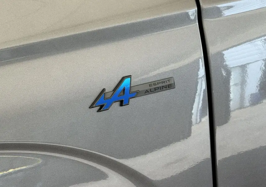 Gros plan sur l'écusson Esprit Alpine bleu sur la porte gris foncé d'un Renault Espace 2025 hybride.