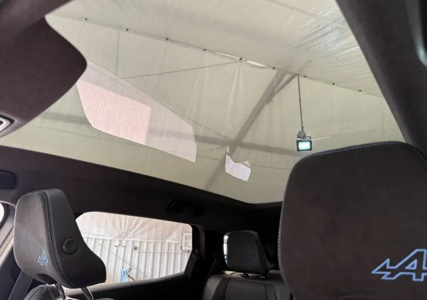 Vue intérieure du toit panoramique et des sièges avant noirs avec logo Alpine bleu sur un Renault Espace gris foncé.