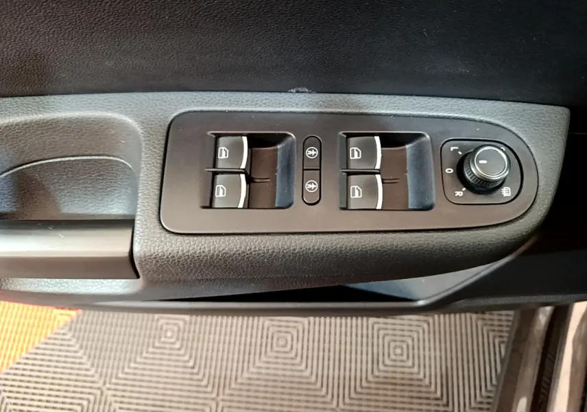 Gros plan sur les commandes de lève-vitres et réglage des rétroviseurs côté conducteur d'un Volkswagen Sharan marron 2017.